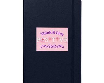Könnte beinhalten: Ein marineblaues Notizbuch mit einem rosa rechteckigen Aufkleber. Der Aufkleber trägt die Worte "Think & Live POSITIVE" in Weiß und Lila, mit floralen und dekorativen Elementen. Das Notizbuch hat ein schwarzes Lesezeichen.