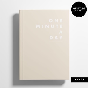 May include: A beige hardcover journal with the text "ONE MINUTE A DAY" in white. A black circle with "GRATITUDE JOURNAL" is in the upper right corner. The word "ENGLISH" is in a black rectangle at the bottom.