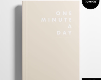 Può includere: Un diario beige con la scritta bianca "ONE MINUTE A DAY". Un cerchio nero con "GRATITUDE JOURNAL" si trova nell'angolo in alto a destra. La parola "ENGLISH" è in un rettangolo nero in basso.