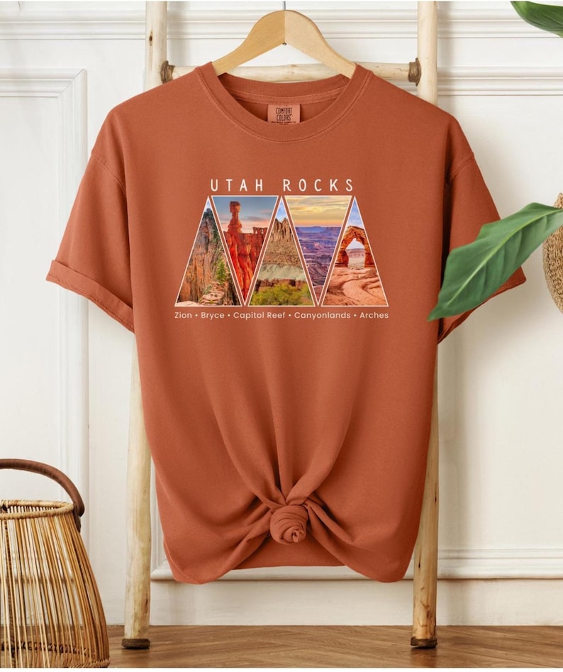 以下が含まれることがあります： さび色のTシャツに、ユタ州の国立公園をそれぞれ描いた5つの三角形が描かれたグラフィックデザインが施されています。三角形の上に「Utah Rocks」という文字が印刷され、その下にザイオン、ブライス、キャピトルリーフ、キャニオンランズ、アーチーズの各公園の名前が記載されています。