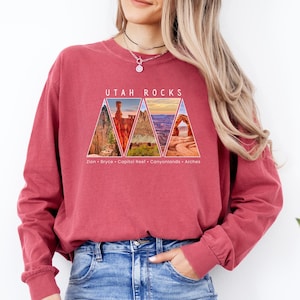 May include: A red long-sleeve shirt with a graphic of a collage of Utah national parks, including Zion, Bryce, Capitol Reef, Canyonlands, and Arches. The text "Utah Rocks" is printed above the graphic.