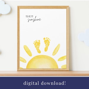 以下が含まれることがあります： 黄色い太陽と、中央に2つの手形が描かれた、印刷可能なデジタルダウンロードです。画像の上部には「You are my sunshine」というテキストがあります。