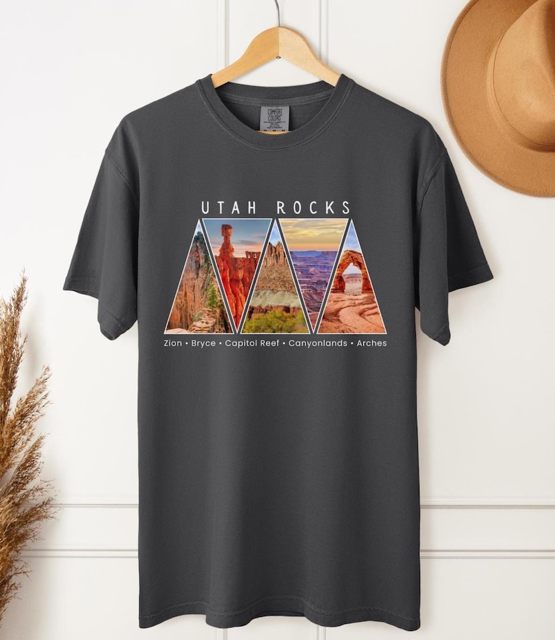 以下が含まれることがあります： 暗いグレーのTシャツに、ユタ州の国立公園の三角形の画像が5つ描かれています。画像の上には「Utah Rocks」という文字が、下には「Zion - Bryce - Capitol Reef - Canyonlands - Arches」という文字が書かれています。
