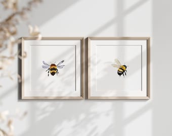 May include: Two framed prints of watercolor paintings of bumblebees. The bee in the left frame is facing the viewer, while the bee in the right frame is flying.