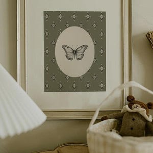 May include: A framed print with a green background and a white oval containing a black and white butterfly illustration. The background has a repeating diamond pattern.