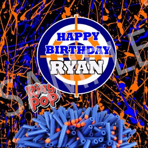May include: A birthday-themed design with a black background featuring blue and orange paint splatters. The design includes a target with "HAPPY BIRTHDAY RYAN" and a pile of blue and orange toy bullets. The words "Ring Pop" are also visible.