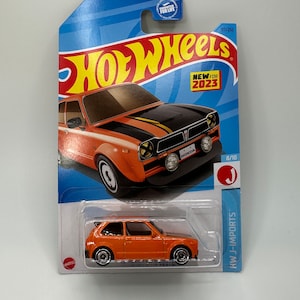 May include: A Hot Wheels die-cast car in orange with black accents. The car is a Honda Civic and is part of the J-Imports series. The packaging is blue and features the Hot Wheels logo and the text "New for 2023".