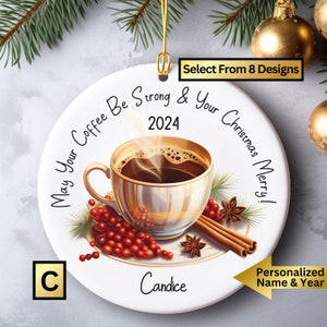 May include: White round Christmas ornament with a gold rim. The ornament features a coffee cup with steam rising from it, surrounded by cinnamon sticks, star anise, and red berries. The text on the ornament reads "May Your Coffee Be Strong & Your Christmas Merry!" with the year "2024" and the name "Candice" below the image.