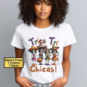 May include: White t-shirt with a graphic of five skeletons dressed in colorful costumes and sombreros. The text "Tricor Tri Chicas!" is printed on the shirt.