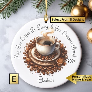May include: White ceramic Christmas ornament with a coffee cup and coffee beans. The ornament has the text "May Your Coffee Be Strong & Your Christmas Merry! 2024" and the name "Elizabeth".