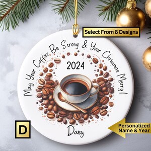 May include: White ceramic Christmas ornament with a coffee cup and coffee beans surrounding it. The text reads "May Your Coffee Be Strong & Your Christmas Merry!" with the year 2024 in the center. The ornament is personalized with the name "Daisy".