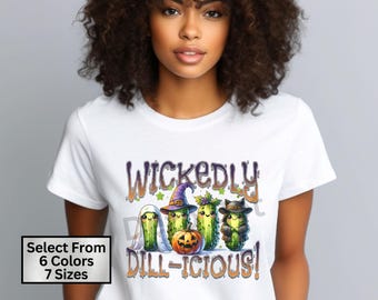 May include: White t-shirt with a graphic of four pickle characters dressed as witches and a pumpkin. The text "Wickedly Dill-icious!" is printed on the shirt.