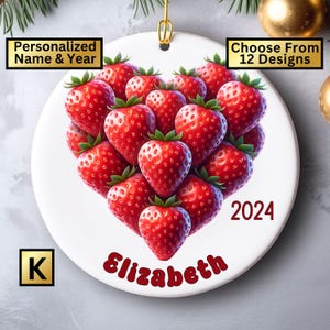 May include: White ceramic ornament with a heart-shaped design made of red strawberries. The ornament is personalized with the name "Elizabeth" and the year "2024".