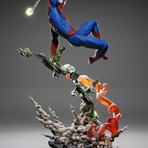 May include: A dynamic figurine of Spider-Man in a classic blue and red suit, leaping into action. He is battling the Green Goblin, who is riding a green glider with orange flames and smoke effects. The base is a rocky terrain.