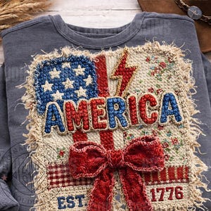 May include: A gray sweatshirt with a patriotic design. The design features the word "AMERICA" in red and blue, a red bow, a blue star field, and the year "1776". The design is stitched onto the shirt.
