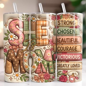 May include: A floral-themed tumbler with a straw, featuring the words "She is Mom" in a patchwork design. The tumbler also includes the words "Strong, Chosen, Beautiful, Courage, Victorious, and Greatly Loved."