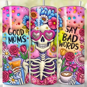 May include: A set of three stainless steel tumblers with a colorful design. Each tumbler features a skeleton with floral accents, heart-shaped sunglasses, and the phrases "Good Moms" and "Say Bad Words". The tumblers are decorated with flowers and other graphics.