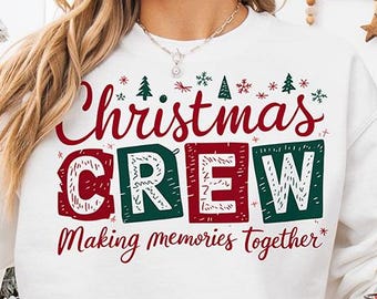 Puede incluir: Una sudadera blanca de manga larga con el texto en rojo y verde Christmas CREW Making memories together, decorada con pequeños gráficos de abetos. La sudadera se acompaña de una taza blanca con un dibujo de Santa Claus.
