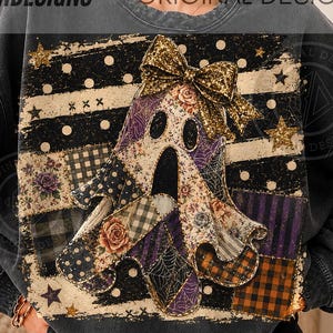 May include: A charcoal grey crewneck sweatshirt featuring a central graphic of a ghost adorned with a gold glitter bow. The ghost is composed of various patchwork patterns including plaid, floral, and spiderweb designs against a striped background.