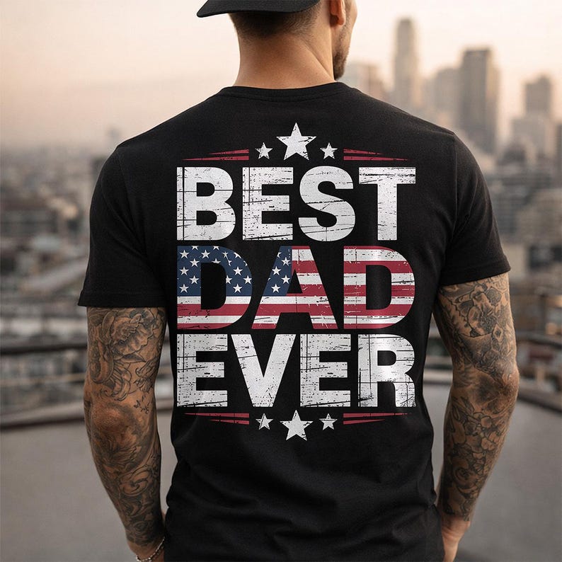 Może przedstawiać: Czarny t-shirt z białym napisem "BEST DAD EVER", z amerykańską flagą w słowie "DAD". Projekt zawiera gwiazdy i czerwone paski. Koszulka ma okrągły dekolt.