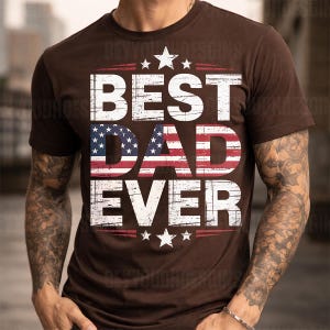 Może przedstawiać: Brązowa koszulka z białym napisem "BEST DAD EVER", z flagą amerykańską w słowie "DAD". Projekt zawiera gwiazdy i czerwone paski, tworząc patriotyczny motyw.