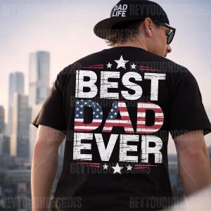 Może przedstawiać: Czarny t-shirt z białym napisem "BEST DAD EVER", z napisem "DAD" wypełnionym wzorem amerykańskiej flagi. Koszulka ma r&oacute;wnież gwiazdy i paski. Widoczna jest czarna czapka z napisem "DAD LIFE".
