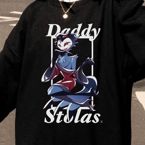 May include: Black sweatshirt featuring the text "Daddy Stolas" with a cartoon illustration of a character in red, blue, and white. The sweatshirt has a crew neck and long sleeves. A can of beverage is held in the left hand.