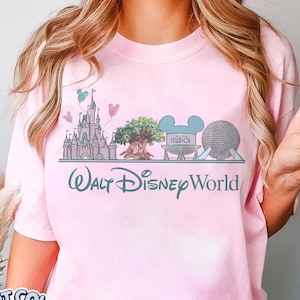 May include: Pink t-shirt with a graphic of Walt Disney World landmarks, including a castle, tree, and Spaceship Earth. The text "Walt Disney World" is below the graphic. The shirt also has the text "Comfort Colors Blossom" in a circle.