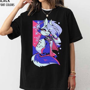 May include: A black short-sleeve t-shirt featuring a graphic print of a stylized anthropomorphic wolf character with purple and blue fur, wearing a jacket, set against a pink and blue rectangular background with white snowflake accents.
