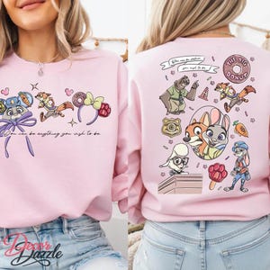 May include: Pink sweatshirt featuring cartoon characters and the text "You can be anything you wish to be." The design includes a bunny, fox, and sloth. The back of the sweatshirt says "THE BIG DONUT."