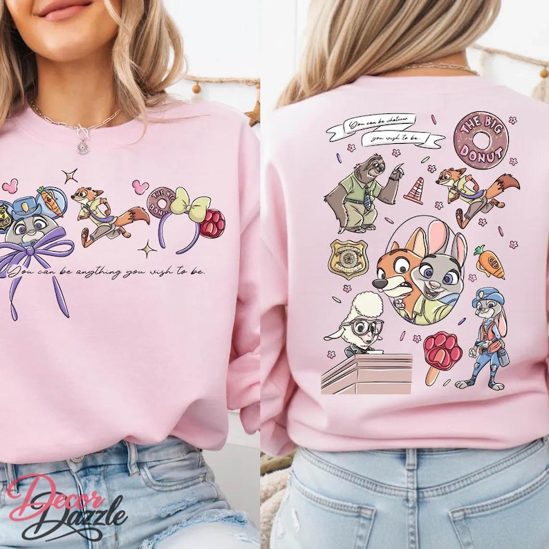 May include: Pink sweatshirt featuring cartoon characters and the text "You can be anything you wish to be." The design includes a bunny, fox, and sloth. The back of the sweatshirt says "THE BIG DONUT."