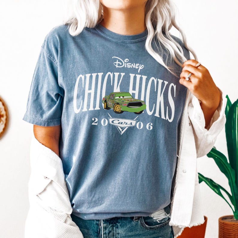 Op de afbeelding: Blauw T-shirt met het Disney Cars-personage Chick Hicks. Het shirt heeft een afbeelding van het personage en de tekst "Chick Hicks 2006 Cars". Het shirt is een korte mouw, ronde hals stijl.