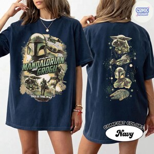 May include: Navy blue t-shirt featuring "The Mandalorian and Grogu" graphic. The front design includes the Mandalorian helmet, Grogu, and text "This is the Way." The back displays various Star Wars elements. "COMFORT COLORS" and "Navy" are also visible.