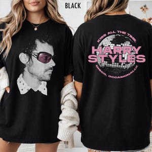 Puede incluir: Camiseta negra con un retrato en blanco y negro de un hombre con gafas de sol. La parte trasera de la camiseta muestra el texto "HARRY STYLES" en rosa, con "KISS ALL THE TIME" y "DISCO, OCCASIONALLY" alrededor de un gráfico de bola de discoteca.