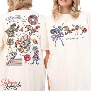 May include: Cream-colored t-shirts with colorful cartoon graphics. One shirt features characters and text: "You can be whatever you wish to be." The other shirt has a similar design with the text: "You can be anything you wish to be."