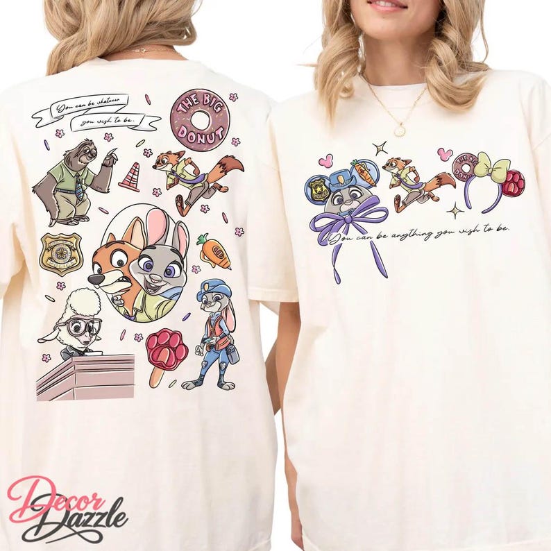 May include: Cream-colored t-shirts with colorful cartoon graphics. One shirt features characters and text: "You can be whatever you wish to be." The other shirt has a similar design with the text: "You can be anything you wish to be."