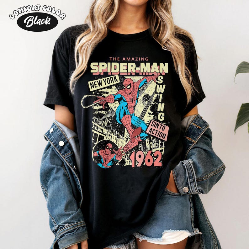 May include: Black t-shirt featuring a vintage Spider-Man graphic. The design includes the words "The Amazing Spider-Man," "New York," and "1962." The graphic shows Spider-Man in action with a cityscape background. The shirt is labeled "Comfort Colors Black."