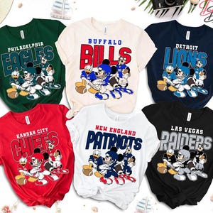 以下が含まれることがあります： NFLチームのロゴと漫画のキャラクターイラストが描かれた、半袖Tシャツ6枚のコレクション。シャツは緑、赤、白、黒など様々な色があります。各シャツにはチーム名とマスコットのデザインが表示されています。