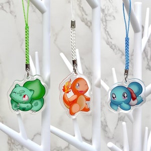 May include: Three clear plastic keychains with different Pokemon characters. The first keychain features a green Bulbasaur, the second keychain features an orange Charmander, and the third keychain features a blue Squirtle.