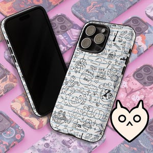 May include: A black smartphone with a white case featuring a doodle design, including the text "PUNK REC" and various cartoon illustrations. The phone is set against a pink background with other phone cases.