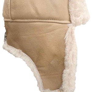 May include: Tan sheepskin aviator hat with ear flaps and a chin strap. The hat has a faux fur lining.