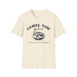 May include: Off-white t-shirt with a vintage-style graphic. The design includes the words "CAMEL TOW & Recovery" and a tow truck illustration. The phrase "we'll get you out of tight spots" is printed below the truck.