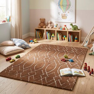 May include: A rectangular brown area rug featuring a white geometric pattern of interconnected diamonds and ovals. The rug is placed on a light-colored wooden floor in a room with toy storage cubes, a wall print, and various scattered children's toys.