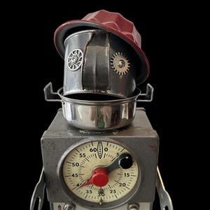 May include: A quirky sculpture crafted from recycled kitchenware. It includes a red hat, a metal pot, and a vintage timer with the text "TIME-O-LITE". The timer has a red knob and a numbered dial.
