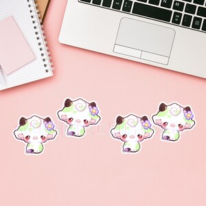 Puede incluir: Cuatro pegatinas de vaca blancas y verdes con flores moradas. Las pegatinas est&aacute;n sobre un fondo rosa.