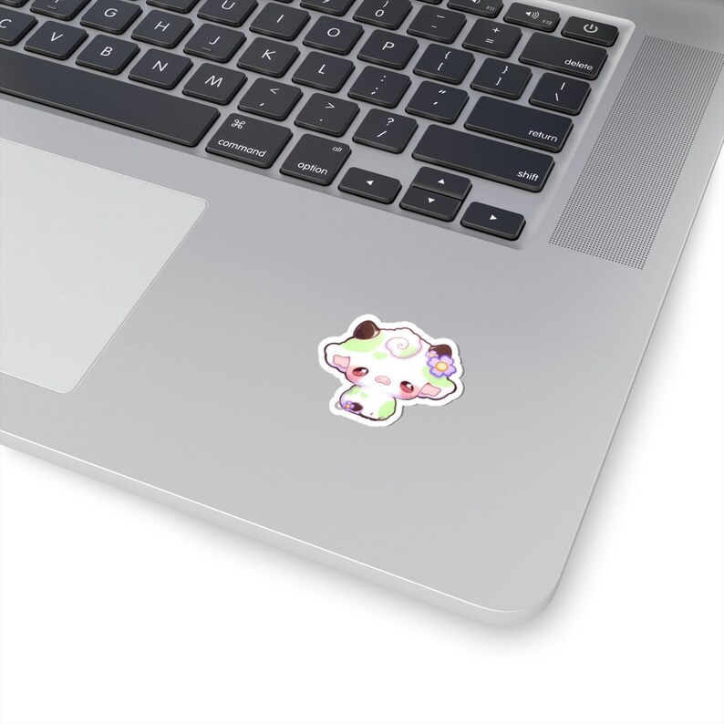 Puede incluir: Una pegatina con una vaca de dibujos animados con manchas verdes y blancas, mejillas rosadas y una flor morada en la cabeza.