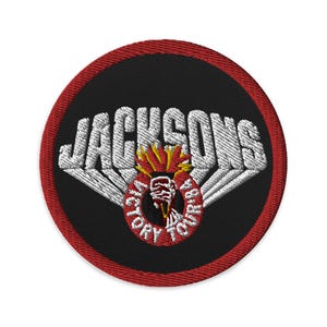 May include: Circular embroidered patch with a black centre, red border, and white text. The text "JACKSONS" arches across the top. A circular emblem in the centre reads "VICTORY TOUR '84". The emblem features a torch design.