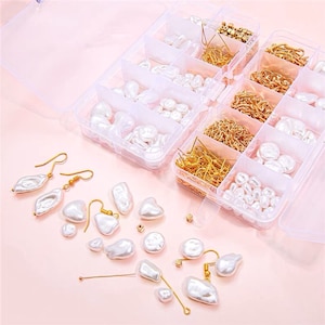May include: A clear plastic storage box filled with white pearl beads and gold-toned earring hooks and chains. The box is open and some of the beads and hooks are scattered on a pink surface.