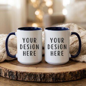 Puede incluir: Dos tazas de cerámica blancas con asas y bordes azul marino. Las tazas tienen el texto "YOUR DESIGN HERE" impreso en negro. Las tazas están sobre una superficie de madera.