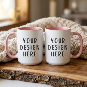 Puede incluir: Dos tazas de cerámica blancas con interior y asas rosas. Las tazas tienen el texto "YOUR DESIGN HERE" impreso en negro. Las tazas se muestran sobre una superficie de madera.